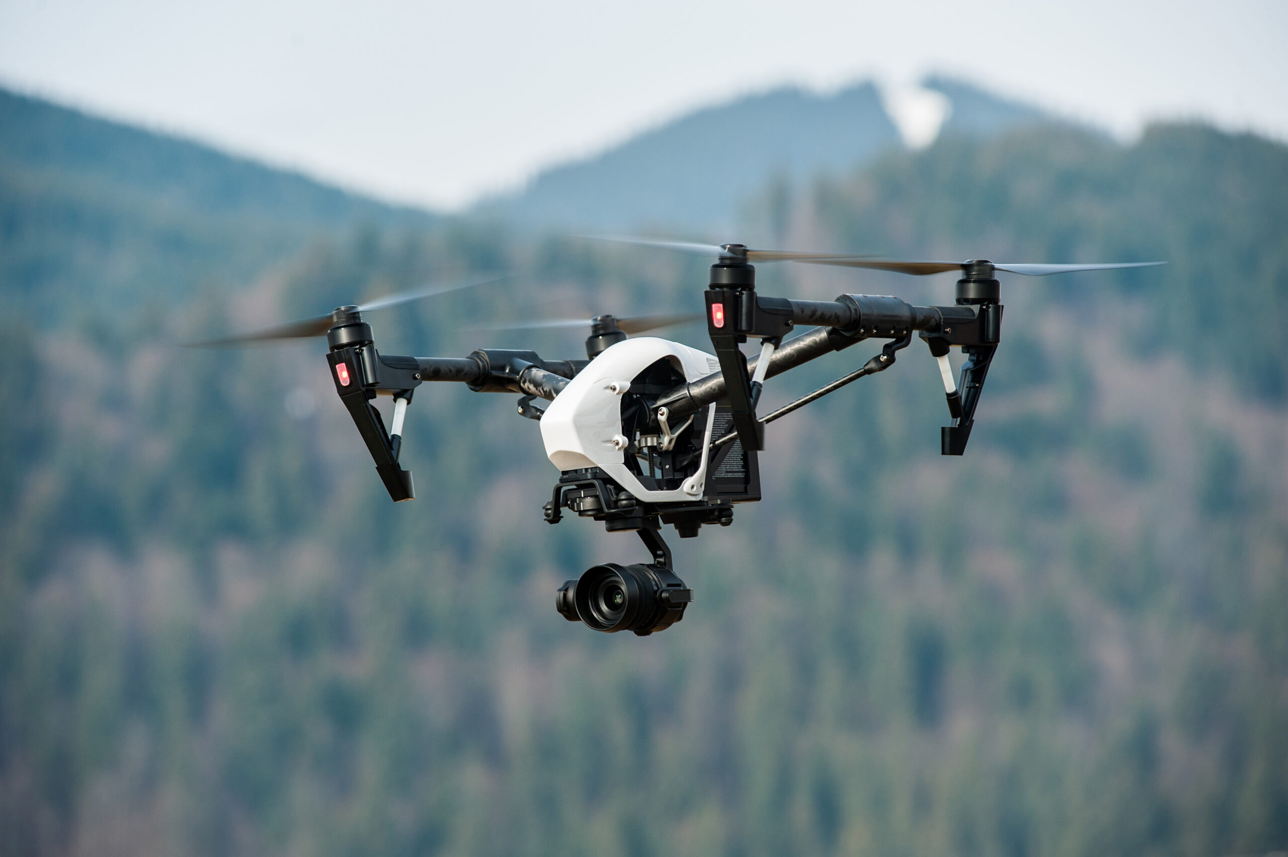 White drone with digital camera flying in sky over mountain